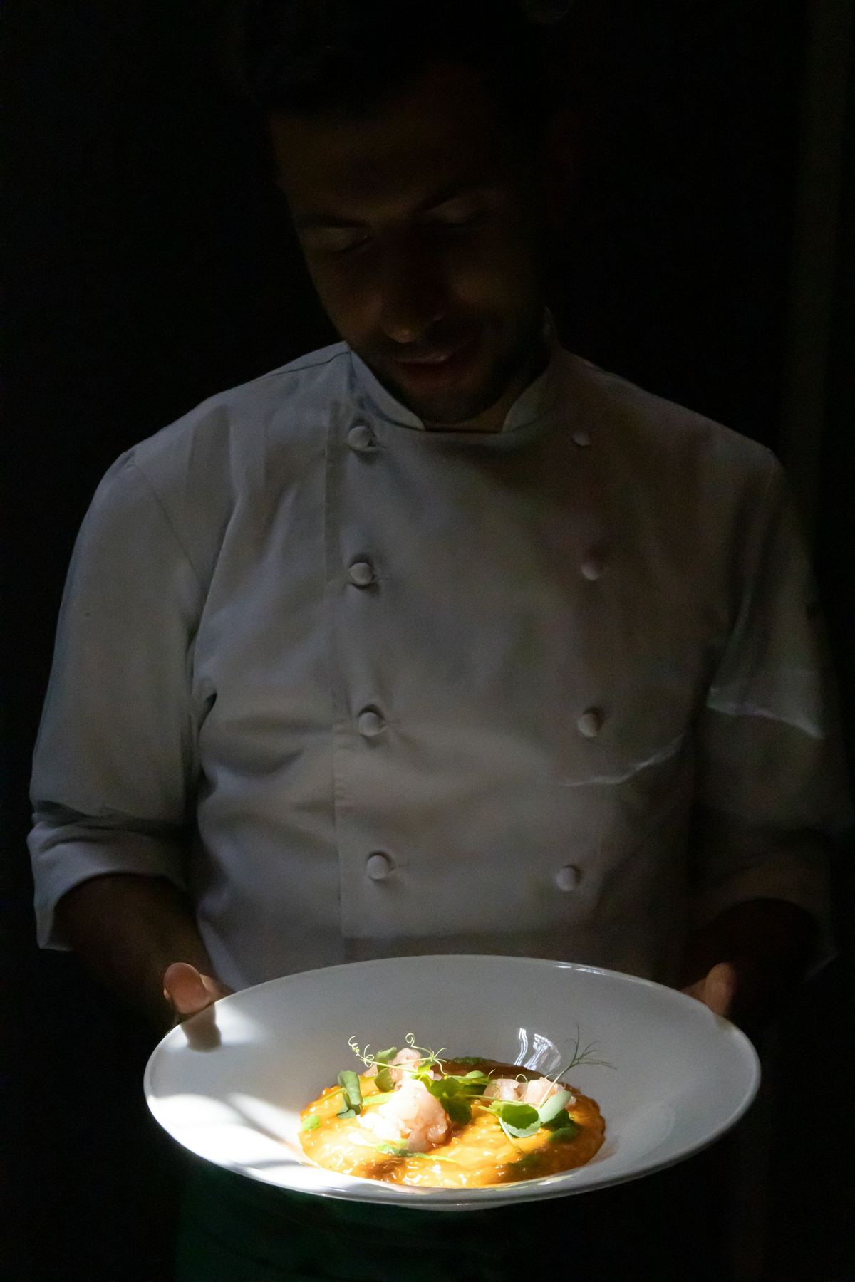 Chef sosteniendo un plato recién emplatado en una cocina en penumbra